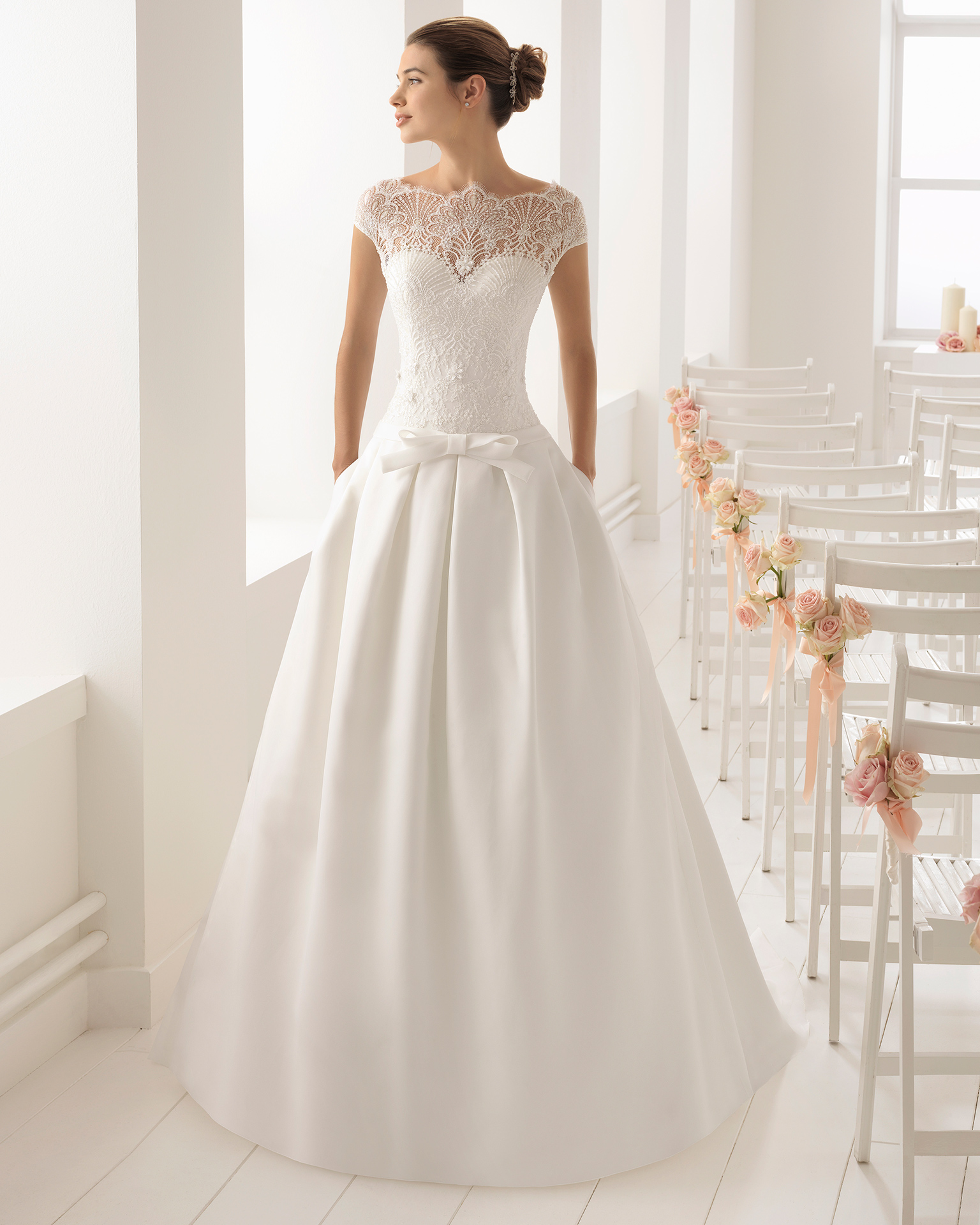 Robe de mariée style romantique en organdi, dentelle et pierreries, avec col illusion et nœud à la taille.